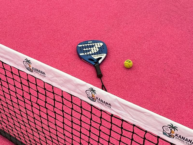 A padel racket and ball by the net on a Kanana court